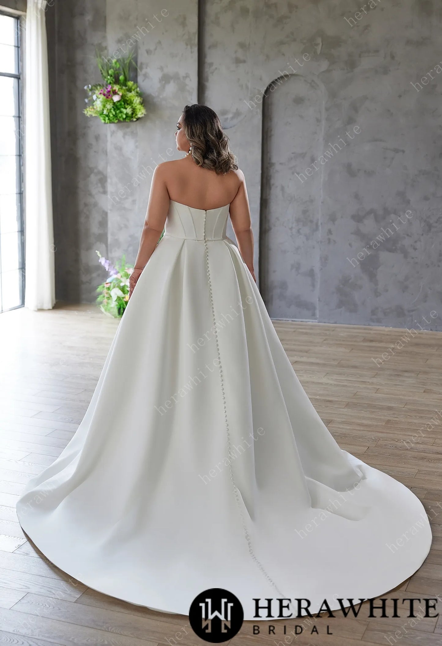 Back view of bride wearing Mattie- Satin Sculpted Strapless A-Line Bridal Gown. Train have trailing buttons