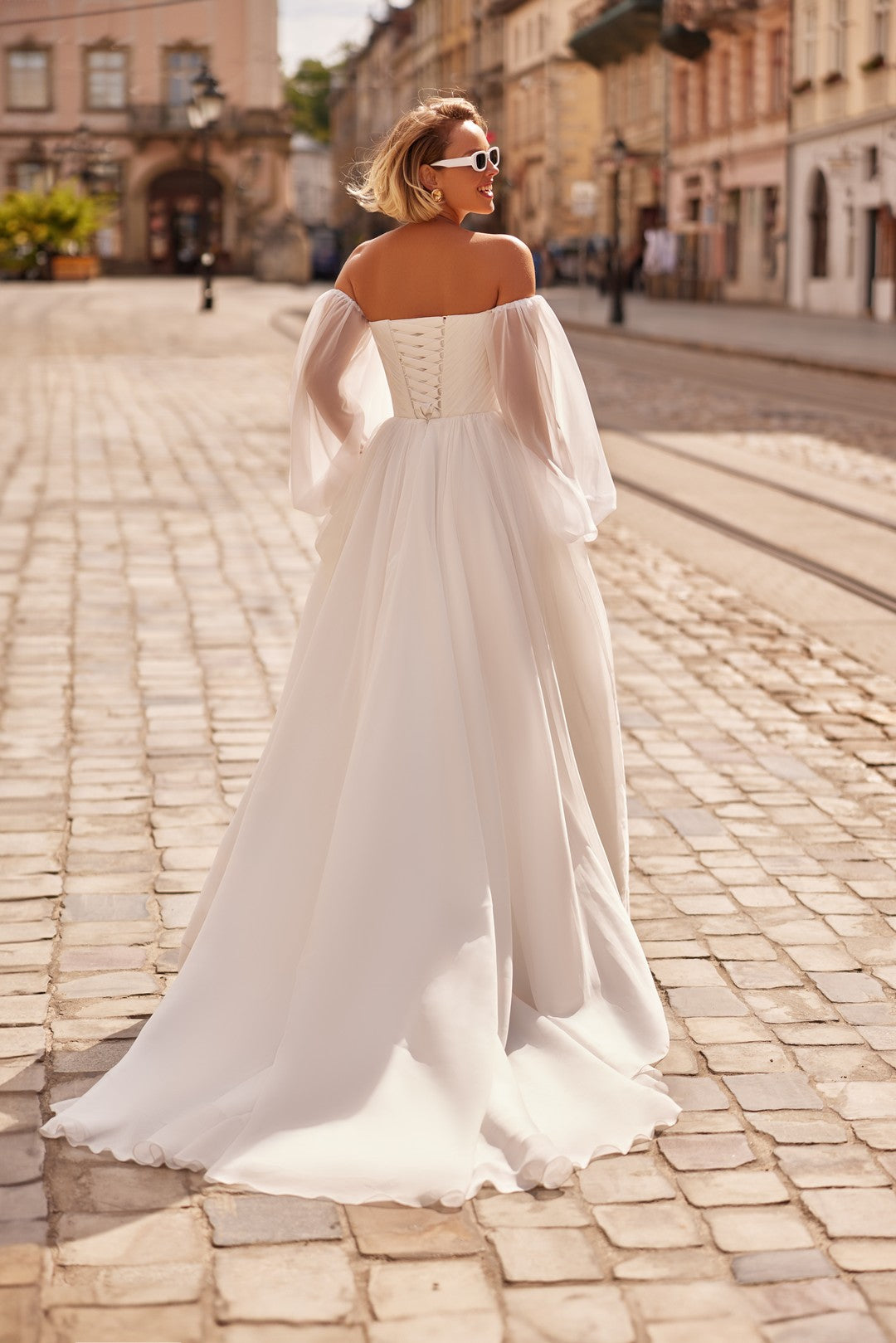 Bride wearing the Petra Wedding Dress – A-Line Bridal Gown with Corset & Sheer Sleeves and chapel train